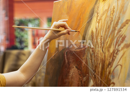 Skilled painter stands before a canvas painting a watercolor rustic artwork. Artist showing her skill and brush technique as she mixes dyes, creating a multicolored masterpiece. Close up. Skilled painter stands before a canvas painting a watercolor rustic artwork. Artist showing her skill and brush technique as she mixes dyes, creating a multicolored masterpiece. Close up. 127891534