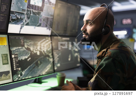 Counterintelligence agency agent relays information from army intelligence analysts to front lines soldiers. Man in camouflage uniform doing satellite communications, talking in mic 127891697