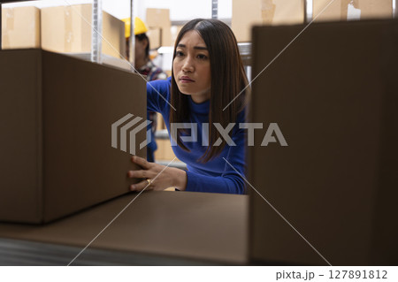 Asian woman preparing custom orders in storage room with parcels and products. Local shipping and retail fulfillment are part of daily business operations in small scale logistics center. Asian woman preparing custom orders in storage room with parcels and products. Local shipping and retail fulfillment are part of daily business operations in small scale logistics center. 127891812