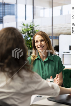 Employer conducting interview with cheerful woman to determine their suitability for company position. Recruiter reviewing happy person resume to determine if necessary qualifications are met Employer conducting interview with cheerful woman to determine their suitability for company position. Recruiter reviewing happy person resume to determine if necessary qualifications are met 127891838