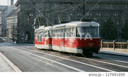 Early morning light highlights a red tram traveling along the tracks near the National Theatre in Prague. The historic architecture creates a scenic backdrop for the lively city. Early morning light highlights a red tram traveling along the tracks near the National Theatre in Prague. The historic architecture creates a scenic backdrop for the lively city. 127891899