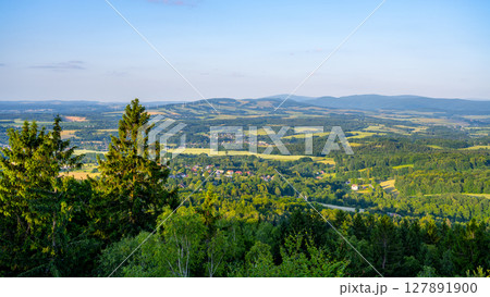 Witness the breathtaking sunset from Popov Cliffs in the Lusatian Mountains. The vibrant colors paint the sandstone rocks, creating a serene evening atmosphere over the lush landscape. 127891900