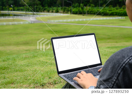 Woman working on laptop with blank screen outdoors in a green park. Technology lifestyle concepts 127893250