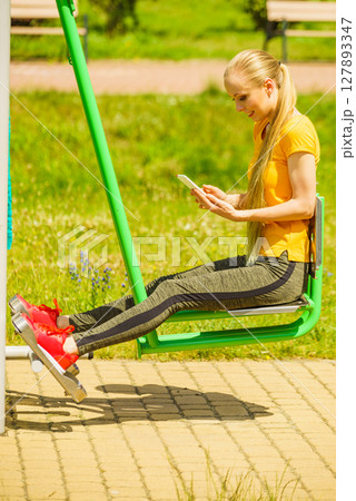 Girl doing exercises outdoor, holding phone Girl doing exercises outdoor, holding phone 127893347