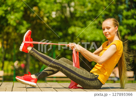 Girl doing exercise outdoor, using resistance fit band. 127893366