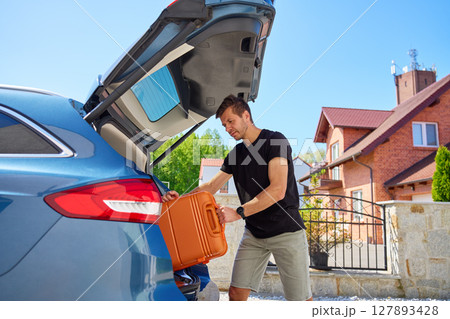 Man placing suitcase into car trunk before summer trip Man placing suitcase into car trunk before summer trip 127893428