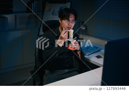 Male employee having a quick meal while working overtime on important projects in the office 127893446