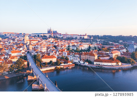 Morning light casts a warm glow over Prague, illuminating the cityscape and medieval architecture of Hradcany and the iconic Charles Bridge. A peaceful view of the city at dawn. 127893985