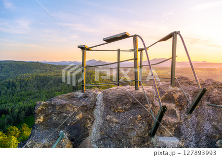 Enjoy a breathtaking sunset over the Lusatian Mountains from the rocky vantage point of Popov Cliffs. The warm evening light casts a golden hue across the sandstone formations and lush forests. 127893993