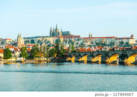 Discover the stunning architecture of Prague Castle overlooking the Vltava River and the iconic Charles Bridge. This clear day showcases the city's historical charm and landscape beauty. 127894007