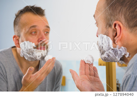 Guy shaving his beard in bathroom Guy shaving his beard in bathroom 127894040