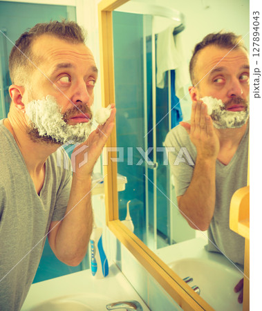 Guy shaving his beard in bathroom Guy shaving his beard in bathroom 127894043