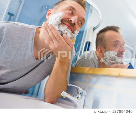 Guy shaving his beard in bathroom Guy shaving his beard in bathroom 127894046