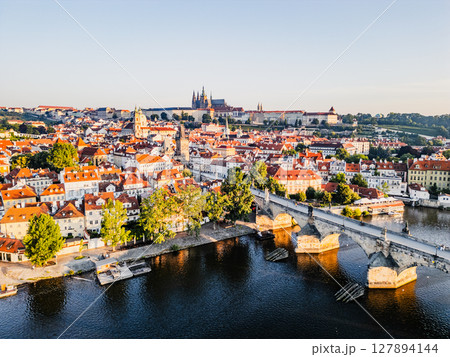 The sky brightens as the sun rises over Prague, casting golden light on the charming medieval architecture. The Vltava River reflects the warm colors, showcasing the iconic Charles Bridge. The sky brightens as the sun rises over Prague, casting golden light on the charming medieval architecture. The Vltava River reflects the warm colors, showcasing the iconic Charles Bridge. 127894144