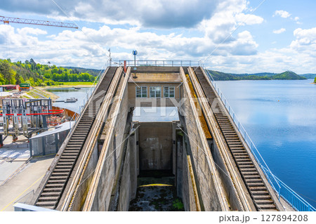 View of the impressive boat lift at Orlik Dam, which efficiently elevates vessels between different water levels. The location features serene water and lush greenery under a partly cloudy sky. View of the impressive boat lift at Orlik Dam, which efficiently elevates vessels between different water levels. The location features serene water and lush greenery under a partly cloudy sky. 127894208