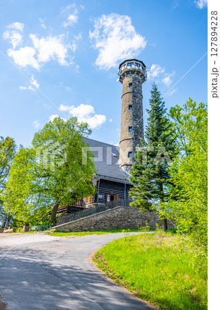 Svatobor lookout tower stands tall against a blue sky, surrounded by lush green trees. A well-maintained path leads to this popular tourist attraction in the serene countryside. 127894228