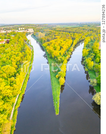 Aerial view showcases the meeting point of Vltava and Labe rivers, surrounded by lush greenery near Melnik. The natural landscape highlights the river bends and vibrant foliage. 127894236