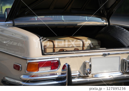 A vintage car trunk opened to reveal a vintage suitcase, evoking the sense of travel and elegance. The image highlights the blend of retro automotive design and nostalgic travel elements. 127895236