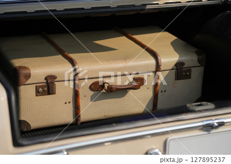 A vintage car trunk opened to reveal a vintage suitcase, evoking the sense of travel and elegance. The image highlights the blend of retro automotive design and nostalgic travel elements. A vintage car trunk opened to reveal a vintage suitcase, evoking the sense of travel and elegance. The image highlights the blend of retro automotive design and nostalgic travel elements. 127895237