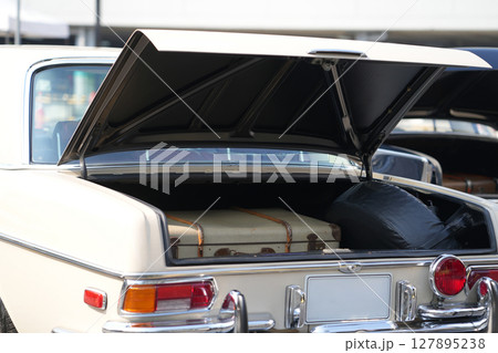 A vintage car trunk opened to reveal a vintage suitcase, evoking the sense of travel and elegance. The image highlights the blend of retro automotive design and nostalgic travel elements. 127895238