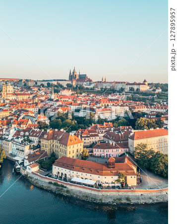 A stunning aerial view of Prague Castle towering above the picturesque Lesser Town, with the Vltava River gracefully flowing through the vibrant cityscape during golden hour. A stunning aerial view of Prague Castle towering above the picturesque Lesser Town, with the Vltava River gracefully flowing through the vibrant cityscape during golden hour. 127895957