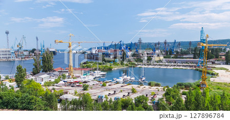 Vivid view of a seaport featuring cranes, docked boats, and lush greenery 127896784