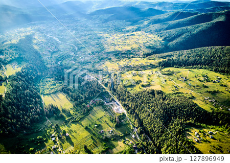 Breathtaking aerial view of valley, bathed in sunlight, with patches of forest and open fields. Winding roads and scattered houses, surrounded by rolling hills and distant mountains. Breathtaking aerial view of valley, bathed in sunlight, with patches of forest and open fields. Winding roads and scattered houses, surrounded by rolling hills and distant mountains. 127896949