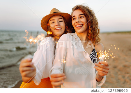 Beautiful Two women holding sparkler celebration on beach. They are having a great time together! Beautiful Two women holding sparkler celebration on beach. They are having a great time together! 127896966
