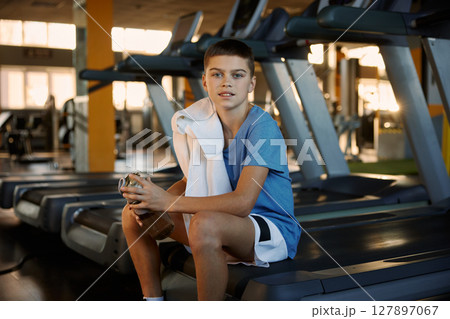Portrait of satisfied teenage boy taking rest after treadmill exercise at gym 127897067