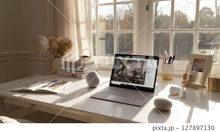 A bright workspace with a laptop on a desk next to a window, filled with sunlight. 127897130