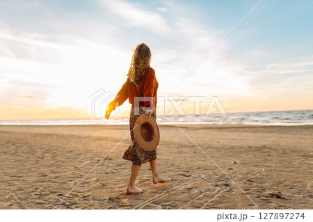 Stylish woman walks at sunset along beach of sea on at sunset. Travel, relax and lifestyle concept. 127897274