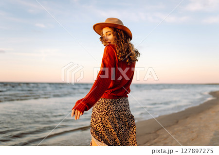 Portrait of a beautiful woman on the beach at sunset. Girl walks along the beach and enjoys weather 127897275