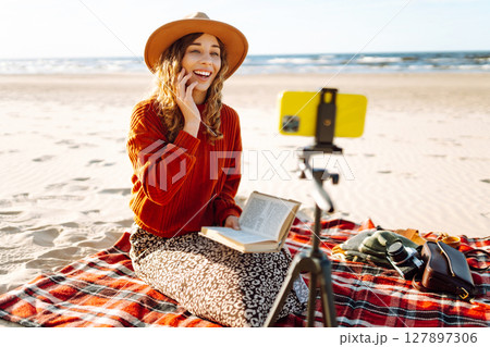 Young woman recording video using smartphone on tripod on the seashore. Travel, blogging concept. 127897306