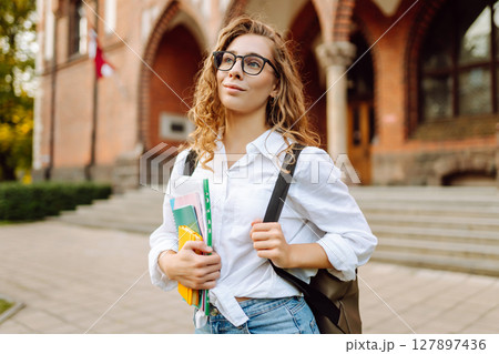 Woman student holds several colorful notebooks, standing outside university. University Student. 127897436