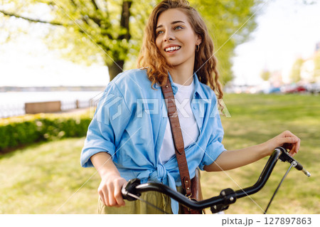 Smiling woman riding bicycle on sidewalk in city spring park. Active urban lifestyle concept. Smiling woman riding bicycle on sidewalk in city spring park. Active urban lifestyle concept. 127897863