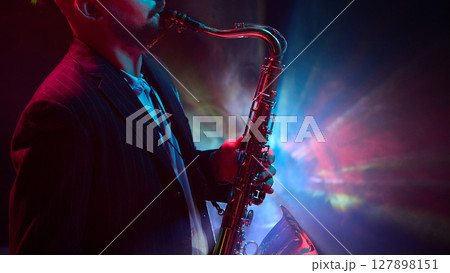 Musician playing saxophone under colorful stage lights in dark moody setting with smoke effect Musician playing saxophone under colorful stage lights in dark moody setting with smoke effect 127898151