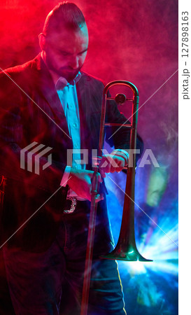 Musician performing with trombone under vibrant stage lights and atmospheric smoke effects Musician performing with trombone under vibrant stage lights and atmospheric smoke effects 127898163