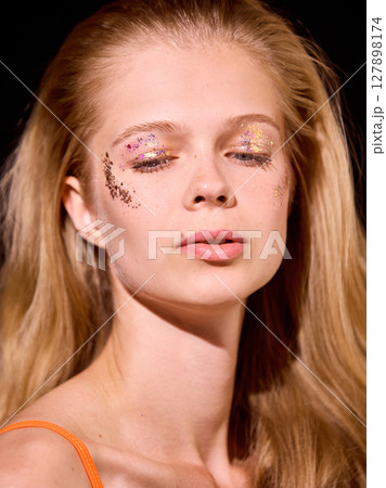 Bold Y2K. Young woman with creative glitter makeup and soft lighting displaying calm expression 127898174