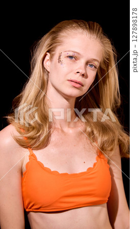 Bold Y2K. Blonde woman with temporary butterfly tattoo wearing orange tank top against black background 127898178
