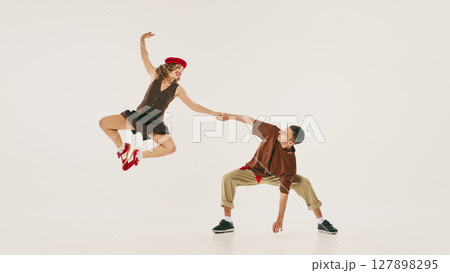 Energetic lindy hop dancers performing high jump in vintage-inspired attire against neutral backdrop 127898295
