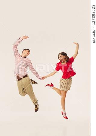 Retro couple energetically dancing lindy hop with joyful expressions and coordinated outfits Retro couple energetically dancing lindy hop with joyful expressions and coordinated outfits 127898325