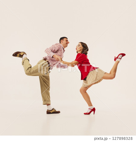 Energetic couple performing lindy hop dance move in vintage 1940s style outfits against plain 127898328
