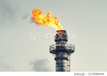 Towering industrial chimney billows fiery gas, filling the sky with thick smoke, a stark reminder of pollution. The steel structure emits dangerous toxins, impacting the air and environment 127898444