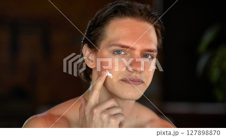 Skin-realism. Smiling man with sun-kissed forehead, shoulders, applying facial moisturizer 127898870