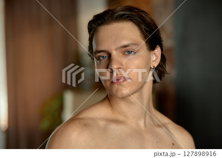 Confident young man with short hair posing indoors against soft blurred background Confident young man with short hair posing indoors against soft blurred background 127898916