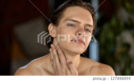 Young man gently applying skincare cream on neck in bright natural setting Young man gently applying skincare cream on neck in bright natural setting 127898954