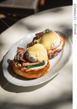 Portion of benedict eggs with sauce and brioche Portion of benedict eggs with sauce and brioche 127899429