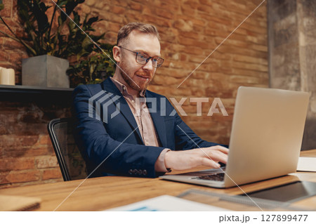 A professional man is skillfully working on his laptop within a contemporary office environment 127899477