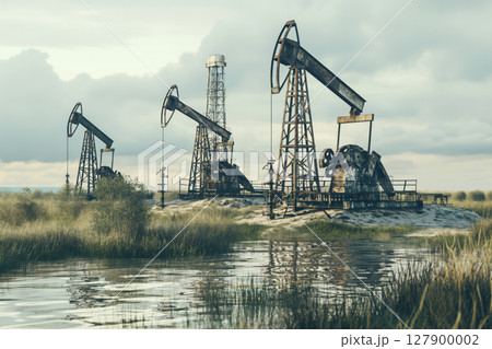 Oil derricks working on the shore of a lake with tall grass and reeds reflecting on the water surface 127900002