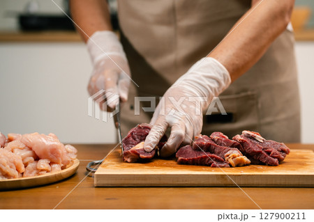 Asian man's hands cutting meat on a wooden cutting board in the kitchen, preparing to cook. Asian man's hands cutting meat on a wooden cutting board in the kitchen, preparing to cook. 127900211